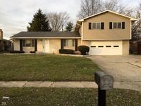 Split-level home featuring beige siding, brick accents, two-car garage, and a well-maintained front lawn at 9016 Neptune Dr, Indianapolis, IN 46229