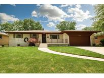 Charming ranch home with a manicured lawn, quaint walkway, and attached garage at 5927 Meadowood Dr, Speedway, IN 46224