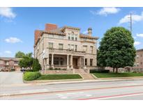 Stately stone home featuring a covered front porch, manicured lawn and mature shade trees at 2105 N Meridian St # 203, Indianapolis, IN 46202