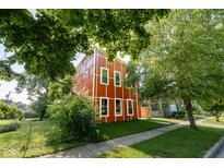 Stylish two-story home with a unique red exterior and white trim, surrounded by lush greenery and a well-manicured lawn at 1210 Churchman Ave, Indianapolis, IN 46203