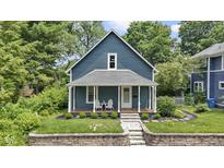 Charming blue two-story home featuring a cozy front porch with white columns and lush landscaping at 6107 Broadway St, Indianapolis, IN 46220