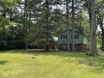 Two-story home with light-blue siding with red brick foundation surrounded by mature trees and a green lawn at 9011 Camby Rd, Camby, IN 46113