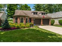 Charming brick home with an attached garage and a beautifully landscaped front yard with colorful flowers at 9520 Settlement W Dr, Indianapolis, IN 46250