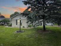 Well-maintained home featuring a green lawn, mature trees, and charming exterior lighting at dusk at 4329 Rutgers Dr # 40B, Anderson, IN 46013