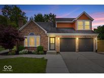Charming brick home features a two-car garage, manicured lawn, and welcoming front entrance at dusk at 9385 Helmsdale Dr, Indianapolis, IN 46256