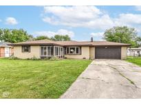 Charming single-story home featuring a brick facade, attached garage, and well-manicured front lawn on a sunny day at 823 Rustic Rd, Anderson, IN 46013