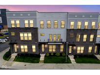 Modern townhome showcasing gray brick and siding, well-lit windows, and manicured landscaping at dusk at 9728 Junction, Fishers, IN 46037