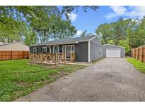 Charming gray home with a wooden porch, well-maintained lawn, and long driveway leading to a detached garage at 5367 Penway St, Indianapolis, IN 46224