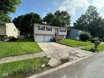Split-level home featuring attached two-car garage and inviting front yard with mature landscaping at 10316 Woodhaven Cir, Indianapolis, IN 46229