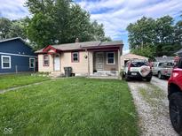 A single-story home with a cozy front yard, gravel driveway, and mature trees against a partly cloudy sky at 1425 Sharon Ave, Indianapolis, IN 46222