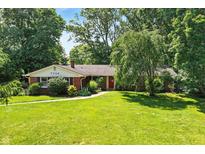 Charming brick home with a well-maintained lawn, mature trees, and a red front door at 7736 Wawasee Dr, Indianapolis, IN 46250