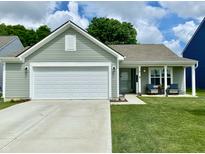 Charming single story home features a two-car garage, covered porch with chairs, and a well-manicured lawn at 213 Drewood Dr, Trafalgar, IN 46181