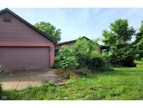 A charming house with a two-car garage is surrounded by overgrown vegetation at 6003 S 125 W, Trafalgar, IN 46181