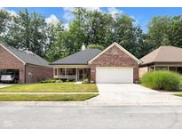 Charming brick home featuring a manicured lawn, front porch, and a two-car garage with a beautiful blue sky overhead at 9735 Woodsong Ln, Indianapolis, IN 46229