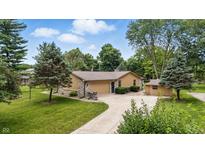Tan single-story home with stone accents, attached garage, mature trees, and a well-manicured lawn at 5982 Oak Hill East Dr, Plainfield, IN 46168