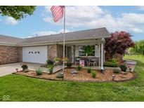 Charming brick home featuring a cozy front porch and landscaped garden, complete with an American flag at 7911 Bentley Commons Dr, Indianapolis, IN 46259