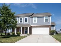 Charming two-story home with light blue siding, brick accents, a well-manicured lawn, and an attached two-car garage at 6218 N Woodside Ct, McCordsville, IN 46055