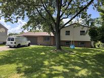 Charming split-level home featuring a brick facade, attached garage, large tree, and a swing in a grassy front yard at 3525 Valley Lake Dr, Indianapolis, IN 46227