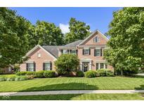 Beautiful two-story brick home with manicured lawn, mature trees, and classic architectural details at 5997 Hollythorn Pl, Carmel, IN 46033