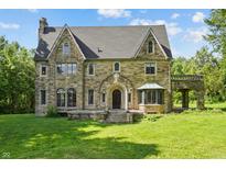 Stately stone home with arched entry, bay window and attached covered patio overlooking manicured front lawn at 2421 W 39Th St, Indianapolis, IN 46228