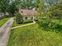 Charming stone cottage-style home with a red front door and lush green lawn and mature trees at 6030 Evanston Ave, Indianapolis, IN 46220