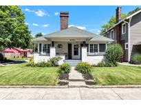 Charming bungalow featuring a landscaped yard, brick chimney, and inviting front porch with flowers at 4721 Carrollton Ave, Indianapolis, IN 46205