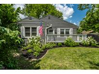 Charming gray home featuring a welcoming front porch, lush landscaping, and an American flag at 5660 Crittenden Ave, Indianapolis, IN 46220