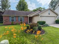 Charming brick home featuring an attached garage, well-manicured lawn, and vibrant flower beds at 9947 Comb Run Ct, Avon, IN 46123