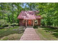 Charming log cabin with a red metal roof, wooden walkway, and surrounded by lush greenery at 3715 Orchard Rd, Columbus, IN 47201