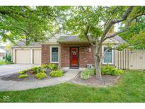 Charming brick home with mature trees, well-manicured lawn, and a welcoming red front door at 11624 Buttonwood Dr, Carmel, IN 46033