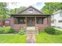 Charming brick home featuring a covered front porch, manicured lawn, and mature landscaping at 5144 N College Ave, Indianapolis, IN 46205