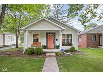 Charming single-story home featuring a inviting porch swing, lush landscaping, and a delightful coral front door at 6142 Evanston Ave, Indianapolis, IN 46220