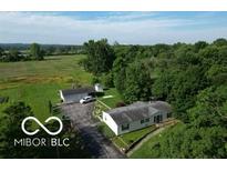 Sprawling property featuring a home, detached garage, and surrounded by lush trees and open fields under a sunny sky at 5387 E County Road 800 S, Mooresville, IN 46158
