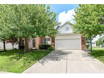 Charming brick home with a two-car garage and mature trees in a well-kept lawn and blue skies overhead at 11820 Stepping Stone Dr, Fishers, IN 46037