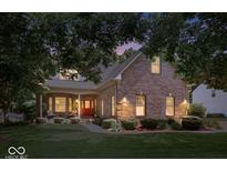 Charming brick home with a cozy front porch and a well-manicured lawn surrounded by mature trees at dusk at 10381 Beaver Ridge Dr, Fishers, IN 46037