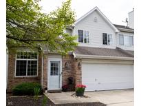 Charming townhome featuring a brick facade, white siding, attached garage and blossoming greenery at 5704 Carrousel Dr, Indianapolis, IN 46254