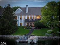 Back view of a luxurious lake house with a boat dock, lush green lawn, and mature trees at 11137 Peppermill Ln, Fishers, IN 46037
