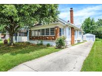 Charming home with a brick chimney, a well-manicured lawn, and a long driveway leading to a detached garage at 1411 N Linwood Ave, Indianapolis, IN 46201