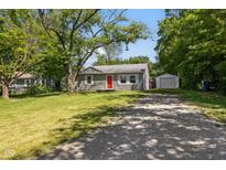 Charming single-story home with a red front door, gravel driveway, and detached garage surrounded by mature trees at 7424 North Dr, Lawrence, IN 46226