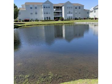 Condos with a pond view, lush green grass, and manicured shrubs on a sunny day at 2276 Essex Dr. # A, Myrtle Beach, SC 29575