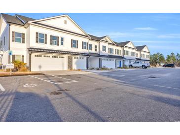 Row of new townhomes with white siding, black shutters, and individual garages in a large parking lot at Lot 40 Lineback Pl. # 40, Longs, SC 29568