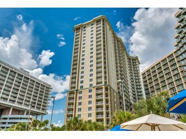 View of the tall condo building with many windows, balconies, and lush tropical landscaping at 9994 Beach Club Dr. # 205, Myrtle Beach, SC 29572