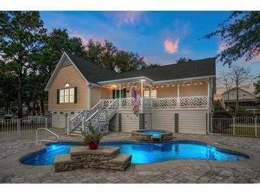 A beautiful backyard with a lit pool and jacuzzi, with a large porch and home behind it at 437 N Boyle Dr., Pawleys Island, SC 29585