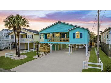 Charming elevated beach house with vibrant blue siding, palm trees, and spacious driveway at 6205 Nixon St., North Myrtle Beach, SC 29582