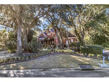 Charming brick home with mature trees and lush landscaping creates a serene and inviting curb appeal at 118 Oatland Lake Rd., Pawleys Island, SC 29585