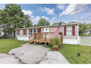 Mobile home with front deck, American flag, and landscaped yard at 3845 Woodridge Circle, Little River, SC 29566