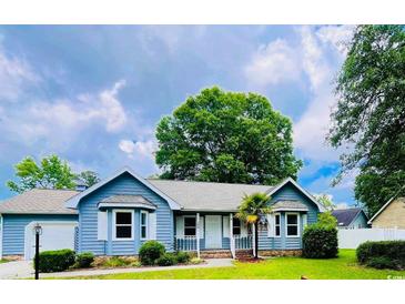 Charming blue home with white trim, a well-manicured lawn, and mature trees under a partly cloudy sky at 104 Willow Ridge Rd., Myrtle Beach, SC 29588