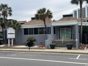 St. John's Inn exterior featuring a gray building, landscaping, and parking at 6803 N Ocean Blvd. # 115, Myrtle Beach, SC 29572