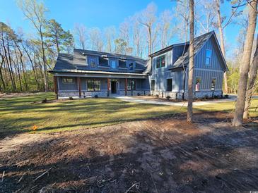 Craftsman-style home with covered porch and stone accents is nestled among tall trees at 8012 Old Reaves Ferry Rd., Conway, SC 29526