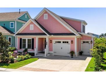 Charming pink home featuring a two-car garage and a well-manicured front yard with lush landscaping at 8217 Sandlapper Way, Myrtle Beach, SC 29572